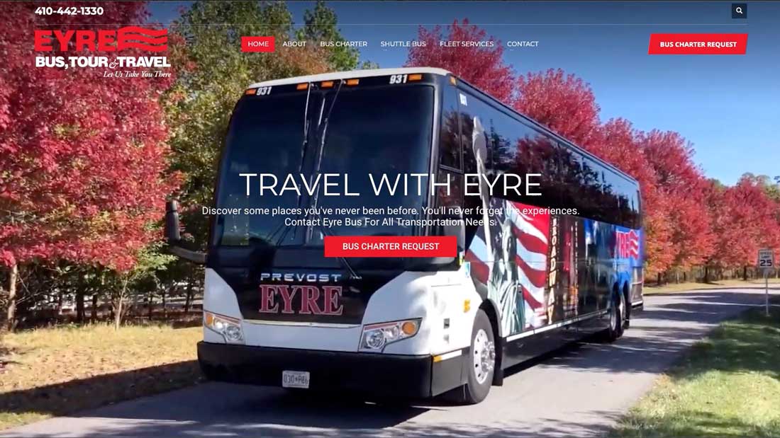 A tour bus with American flag graphics parked on a tree-lined road in autumn.