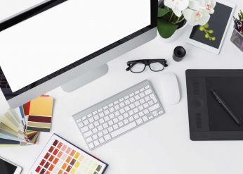 A graphic designer's workstation with a laptop displaying design software, a tablet, and color swatches, representing graphic design services.